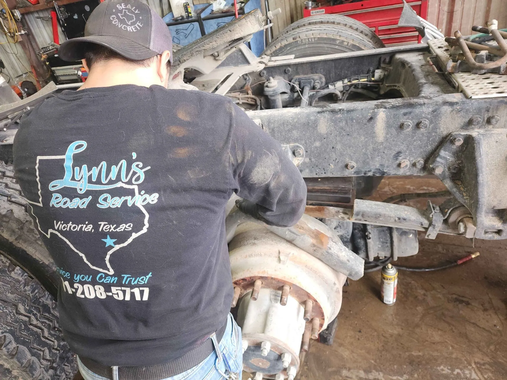 Mechanic working on a truck wheel in the shop wearing a Lynn's Road Service shirt.